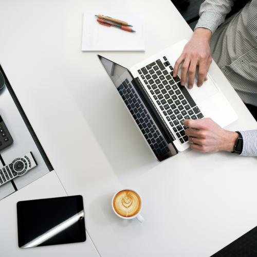 Man at laptop with coffee, pen and notebook wearing business shirt.