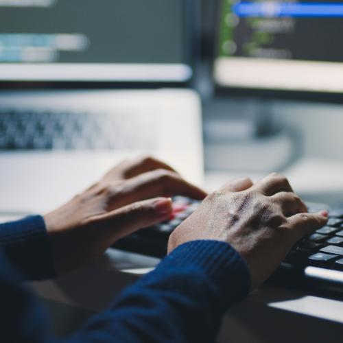 Man at laptop with blurred screens wearing jumper.