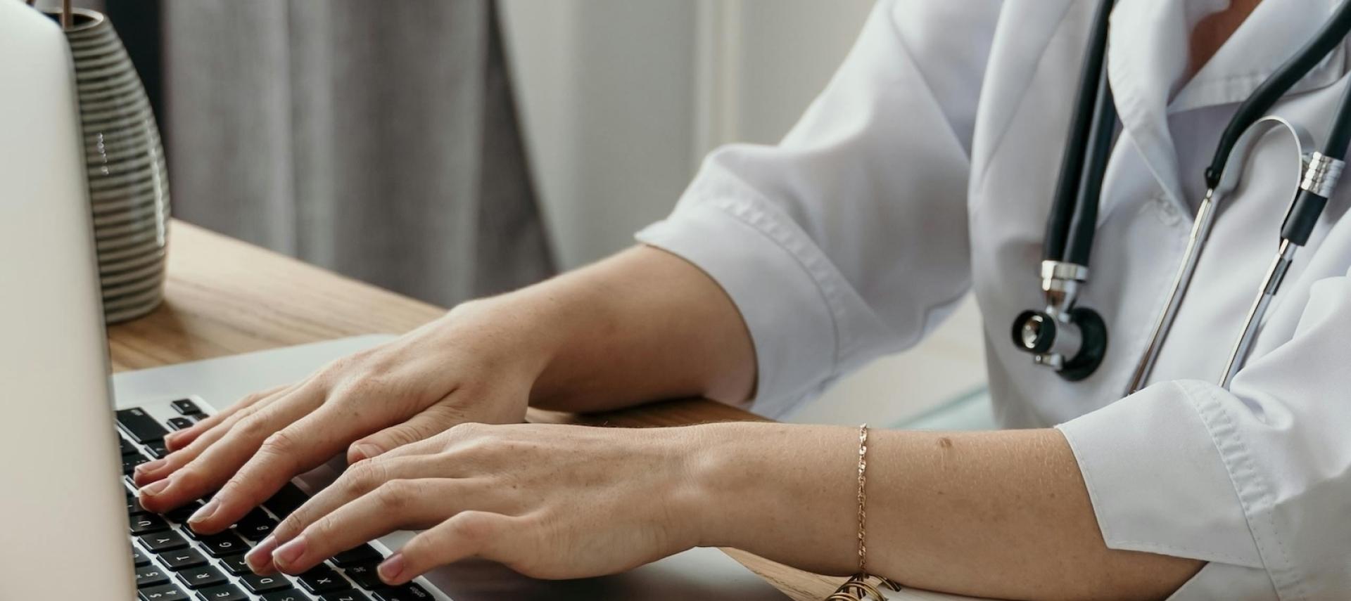 Doctor at laptop with stethoscope around neck.