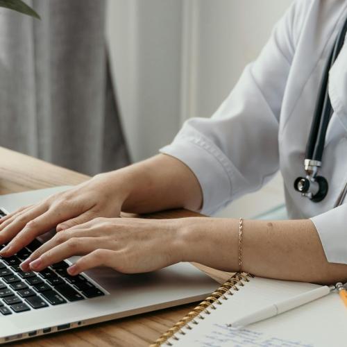 Doctor at laptop with stethoscope around neck.